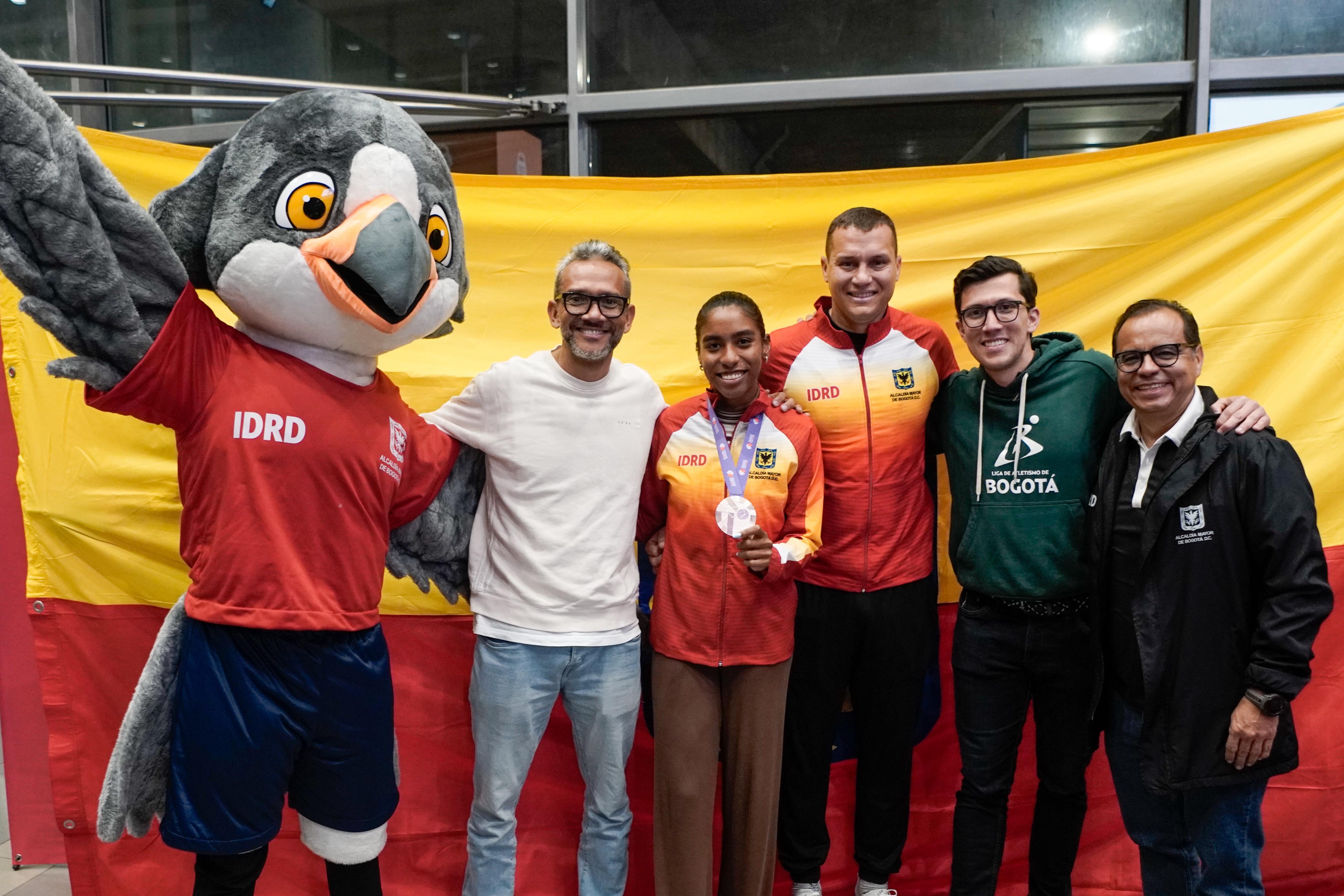 Gran recibimiento a la medallista mundial. Aparecen (izq. a der.) Monse (mascota del Equipo Bogotá), Paulo Villar (presidente Liga de Atletismo), Natalia Linares, Martín Suárez (entrenador), Cristian Alzate (ejecutivo de la Liga) y William Nieto (jefe de Alto Rendimiento del IDRD. Foto IDRD. 